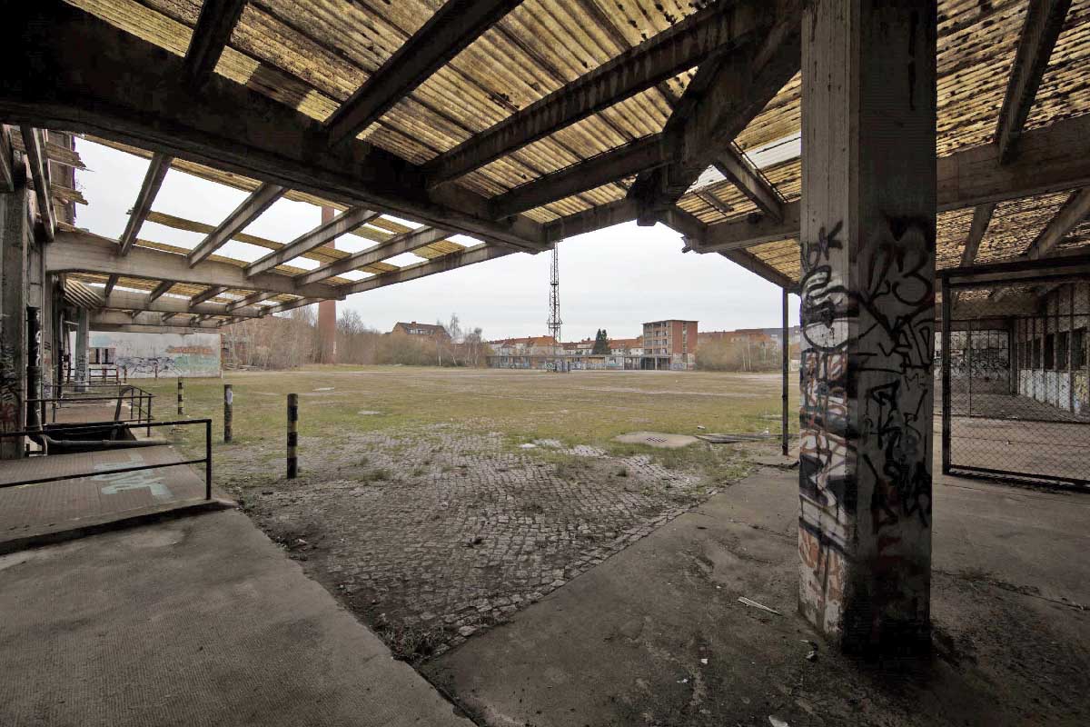 Abb. 1. Schwerin, Mittelweg 7, Kraftfahrzeuginstandsetzungswerk, Blick aus der Reparaturhalle über den Werkplatz nach Südosten, rechts der Bildmitte das moderne Verwaltungsgebäude, daran anschließend der eingeschossige Wasch- und Pflegedienstflügel, links davon über dem Gehölz aufragend das Kultur- und Sozialgebäude in traditioneller Bauform. (LAKD-MV/LD, A. Bötefür, 2015) Abb. 1. Schwerin, Mittelweg 7, Kraftfahrzeuginstandsetzungswerk, Blick aus der Reparaturhalle über den Werkplatz nach Südosten, rechts der Bildmitte das moderne Verwaltungsgebäude, daran anschließend der eingeschossige Wasch- und Pflegedienstflügel, links davon über dem Gehölz aufragend das Kultur- und Sozialgebäude in traditioneller Bauform.