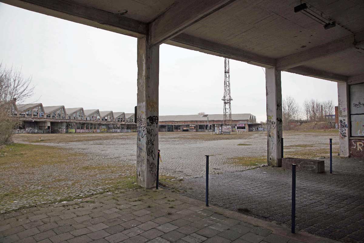 Abb. 8. Schwerin, Mittelweg 7, Kraftfahrzeuginstandsetzungswerk, Blick aus der Durchfahrt über den Werkplatz zur L-förmigen Reparaturhalle mit Sheddachkonstruktion. (LAKD-MV, LD, A. Bötefür, 2015) Abb. 8. Schwerin, Mittelweg 7, Kraftfahrzeuginstandsetzungswerk, Blick aus der Durchfahrt über den Werkplatz zur L-förmigen Reparaturhalle mit Sheddachkonstruktion.